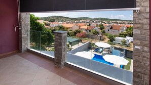 A balcony with a view of a residential area, a swimming pool, and a stone pillar. - Apartments Villa AS Jezera (Tisno)