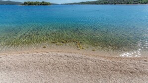 A clear view of a pebble beach leading to a calm sea with a distant island. - Apartments Villa AS Jezera (Tisno)