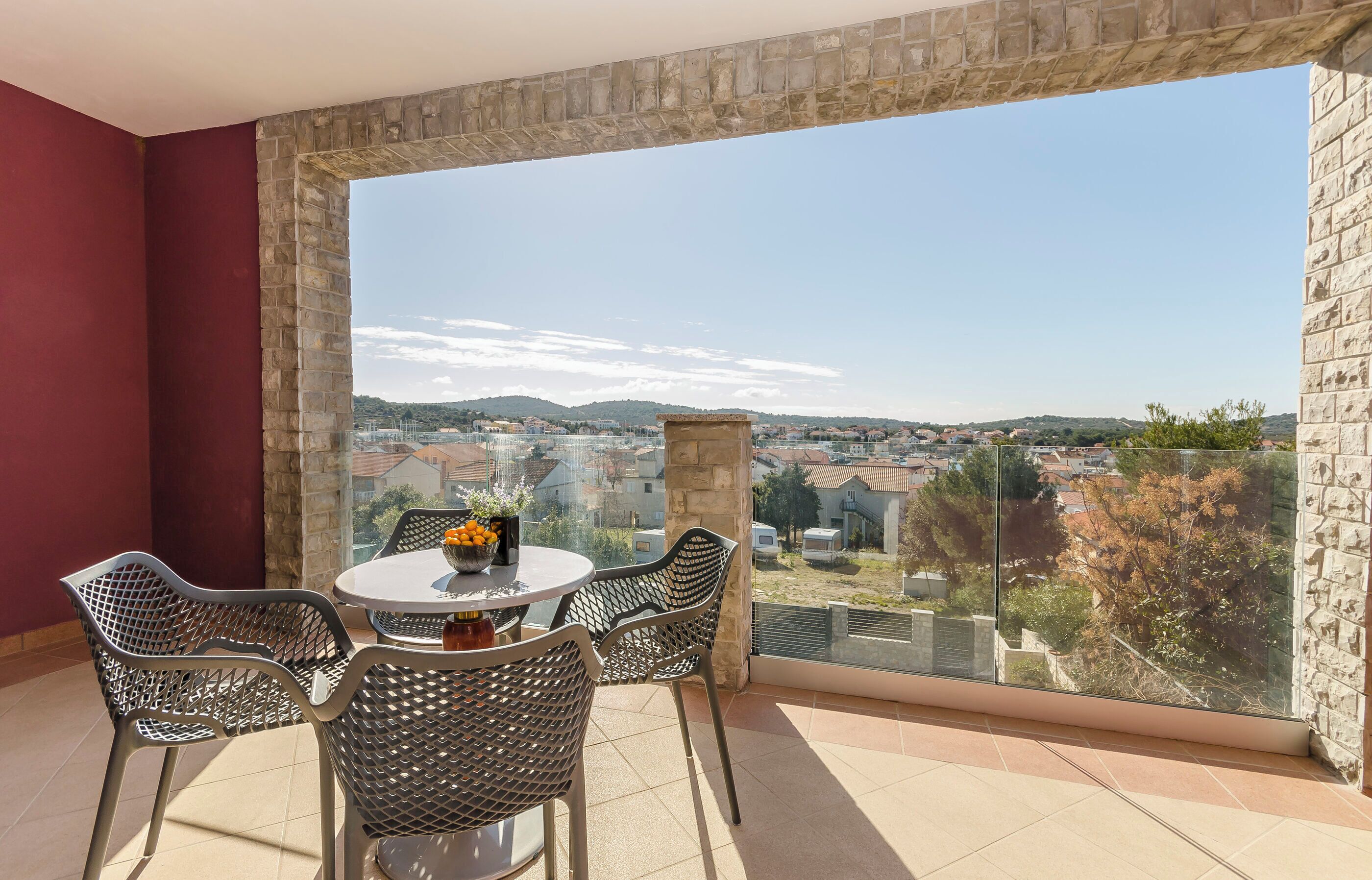 A balcony with a table and chairs, a stone pillar, and a view of a cityscape.