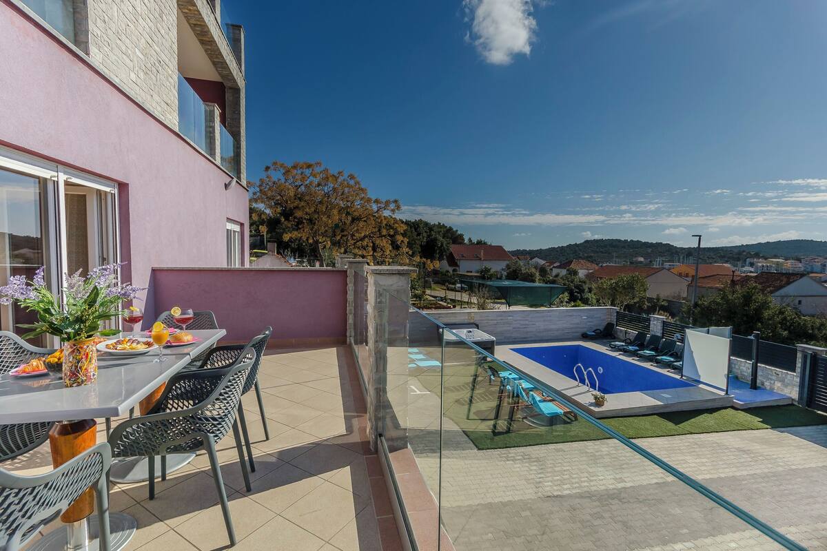 A rooftop terrace with a pool, dining area, and a view of the surrounding landscape.