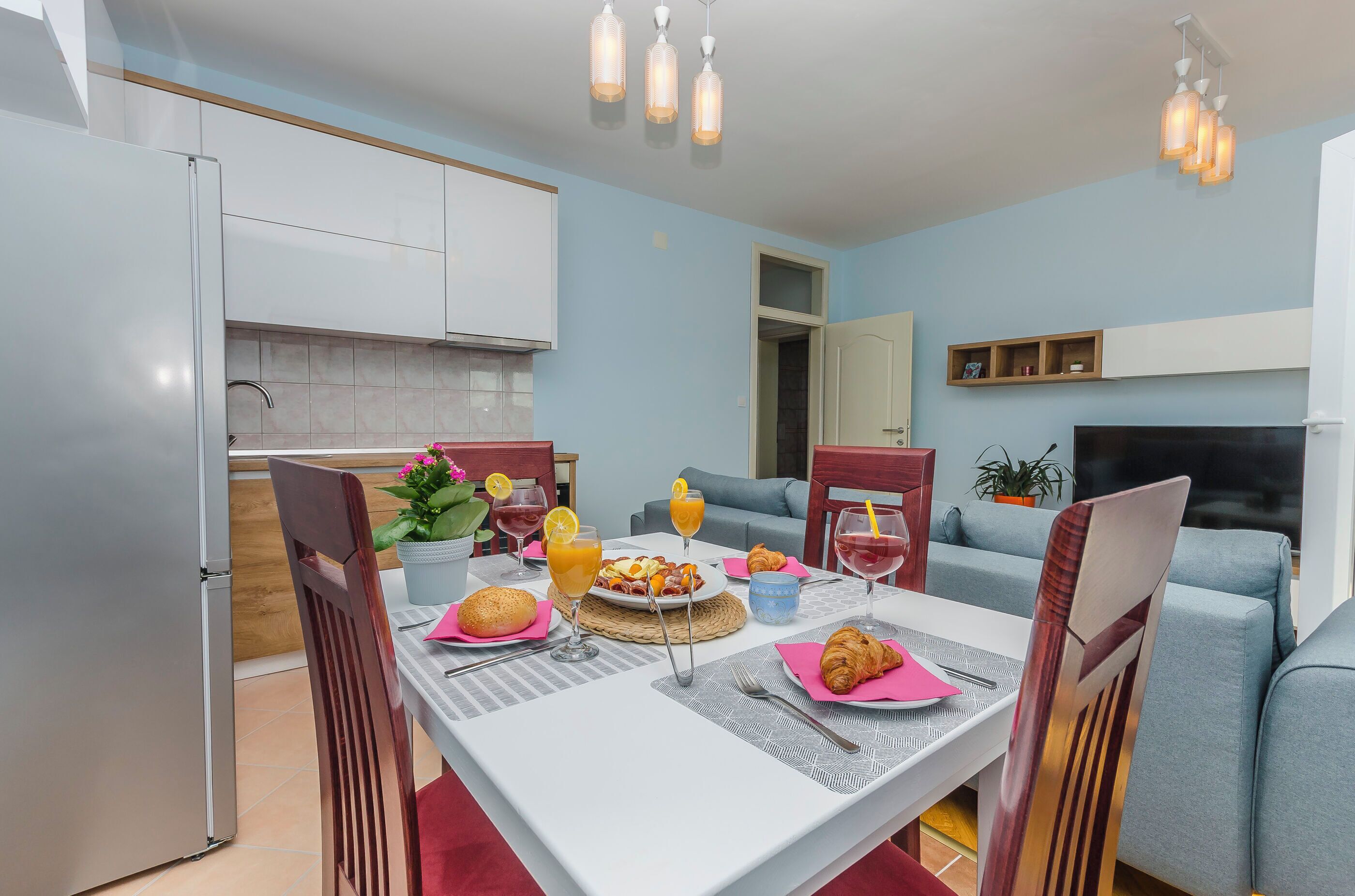 Una cocina moderna con armarios blancos, una mesa de comedor dispuesta para el desayuno y un sofá gris en la sala de estar.