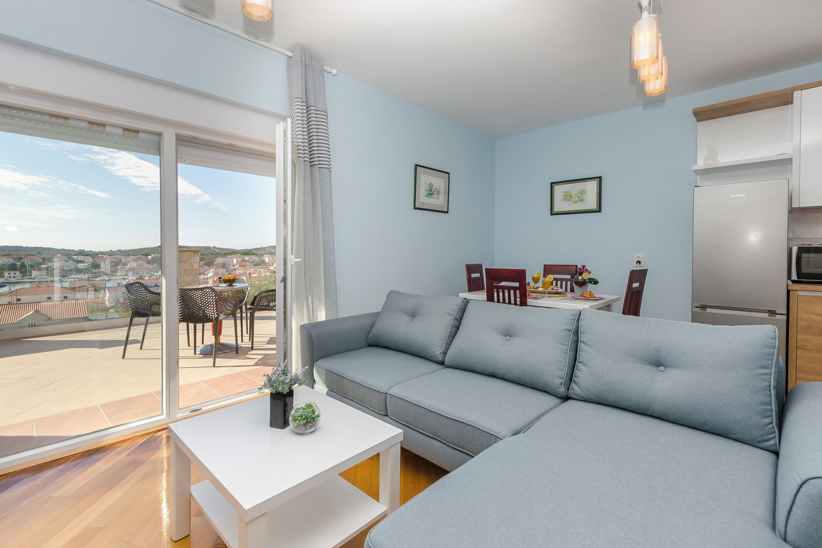 A modern living room with a grey sofa, a white table, and a view of the city through large windows.