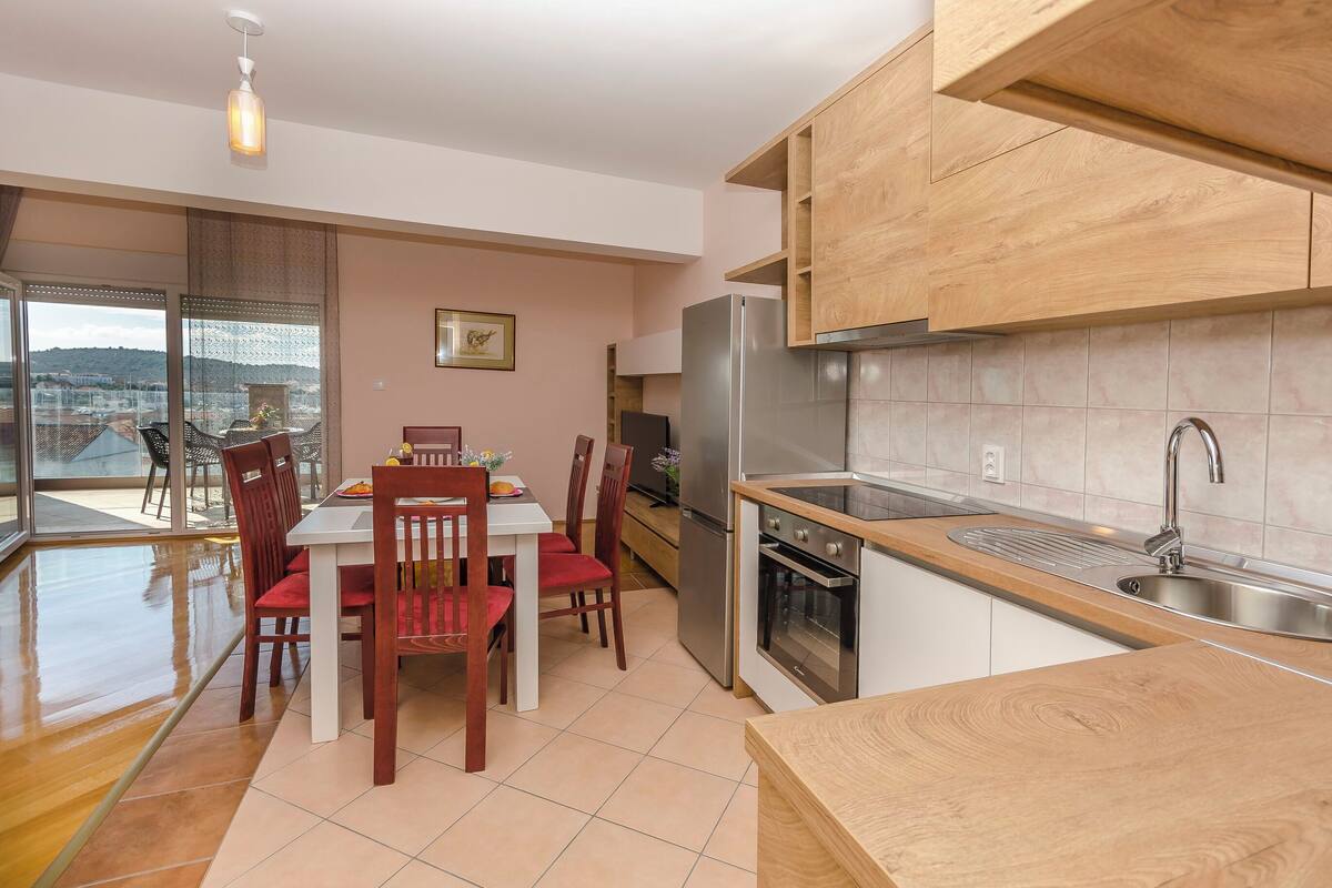 A modern kitchen with wooden cabinets, a stainless steel refrigerator, and a built-in oven.