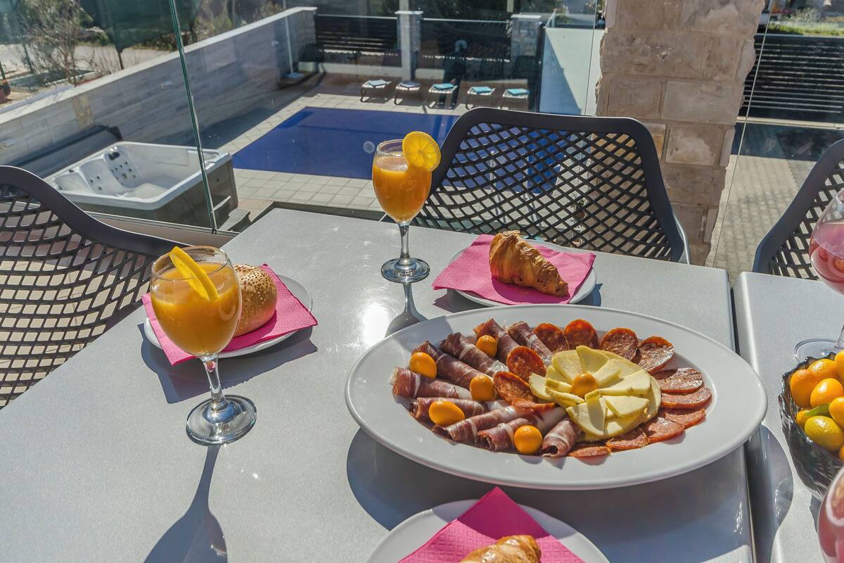 A table with a plate of cured meats, a glass of orange juice, and a croissant.