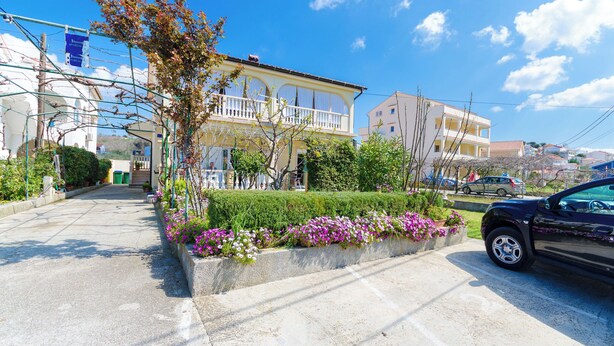 A street view with a building featuring a balcony, a car parked on the side, and a clear blue sky.