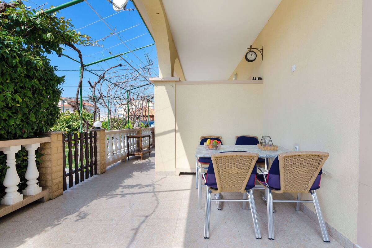 A balcony with a table and chairs, a clock, and a view of the street.