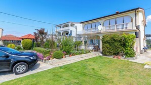 A two-story house with a balcony, surrounded by a well-maintained lawn and potted plants.