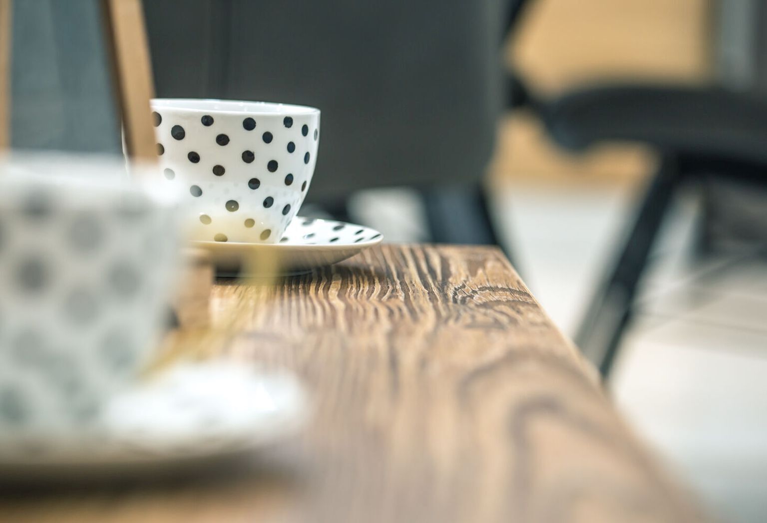 Una taza blanca con lunares negros sobre un plato, sobre una mesa de madera.