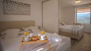Une chambre d’hôtel avec un lit, une table de chevet sur laquelle se trouvent des éléments pour le petit-déjeuner, une grande fenêtre donnant sur la ville et un tableau accroché au mur.