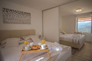 Habitación de hotel con cama, mesita de noche con artículos de desayuno, ventana grande con vista a la ciudad y un cuadro en la pared.