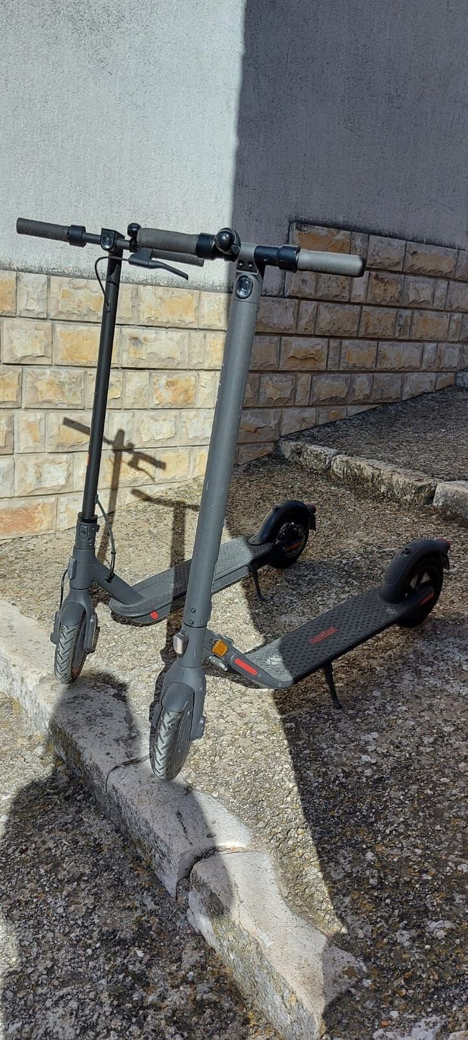 Een stilstaande elektrische scooter geparkeerd op een betonnen rand naast een bakstenen muur.