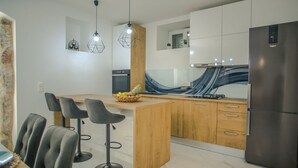 Une cuisine moderne dotée d’un îlot central, de tabourets de bar, d’un réfrigérateur et de luminaires suspendus.