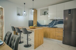 Una cocina moderna con una isla central, taburetes de bar, un refrigerador e iluminación colgante.