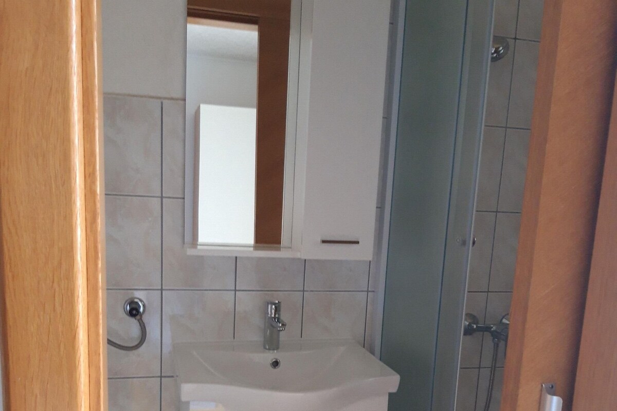 A bathroom with a white sink, mirror, and cabinet, a shower area, and a tiled floor.