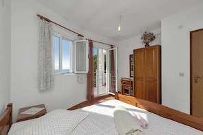 A bedroom with a bed, a wooden wardrobe, a chair, and a window with curtains. - Apartments Robinzon Nikola (Sucuraj)