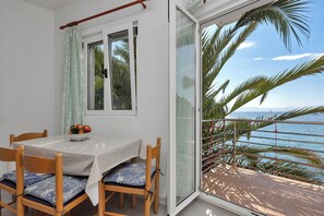Un'area pranzo con tavolo e sedie, una ciotola di frutta e vista sul mare attraverso una porta in vetro.
