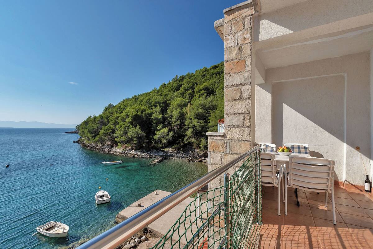 A balcony with a view of the sea, a table with chairs, and a bottle of wine.