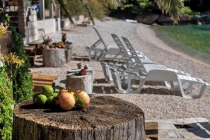 Un tavolo di legno con frutta e una panca con sedie bianche in un'area esterna soleggiata.