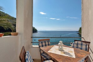 Un balcone con tavolo e sedie, affacciato su un corso d'acqua e una costa lontana.