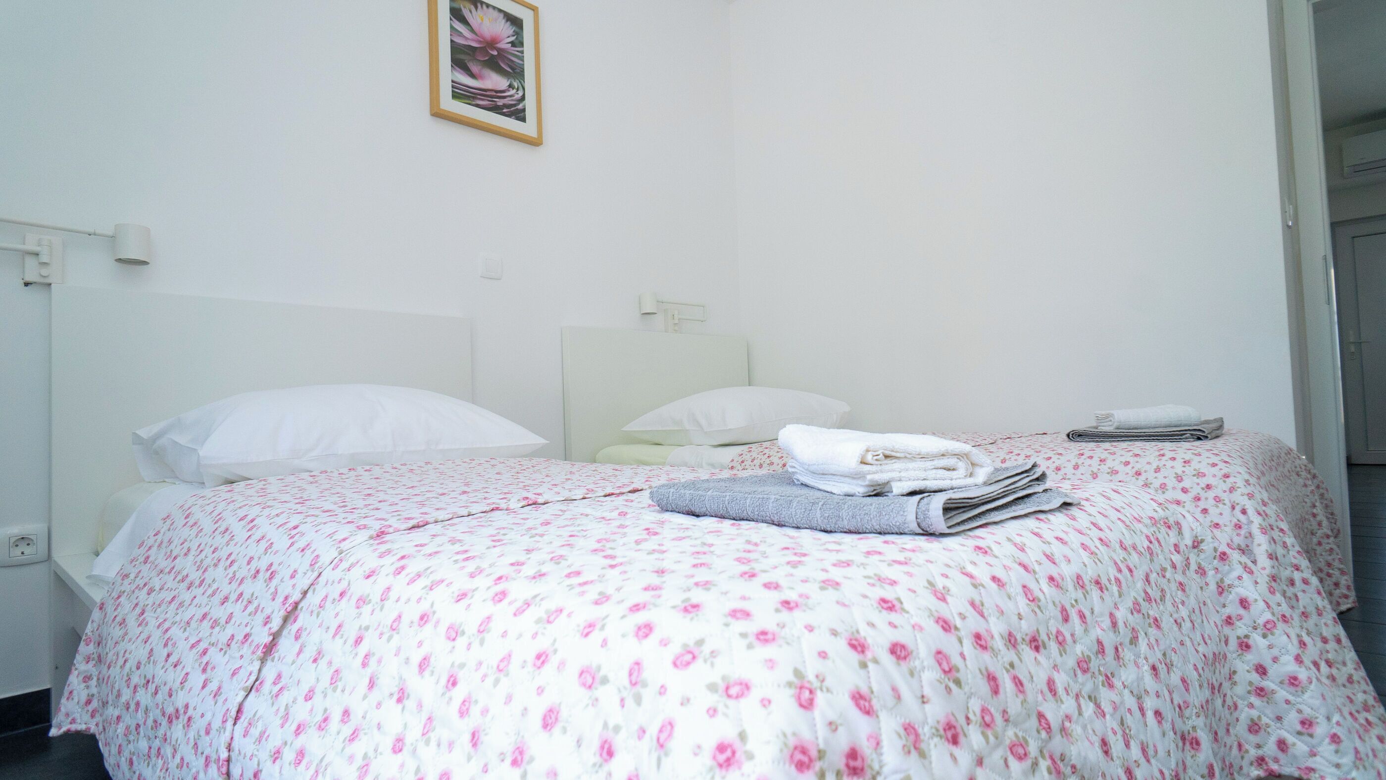 A neatly made bed with a floral bedspread, white pillows, and a folded towel on the side.