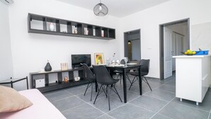 A modern, well-lit room with a dining table, chairs, a TV, and a kitchen area with a sink and counter. - Apartments Annela (Seget)