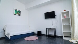 A small, modern room with a bed, a TV mounted on the wall, a small table, and a shelf unit. - Apartments Annela (Seget)