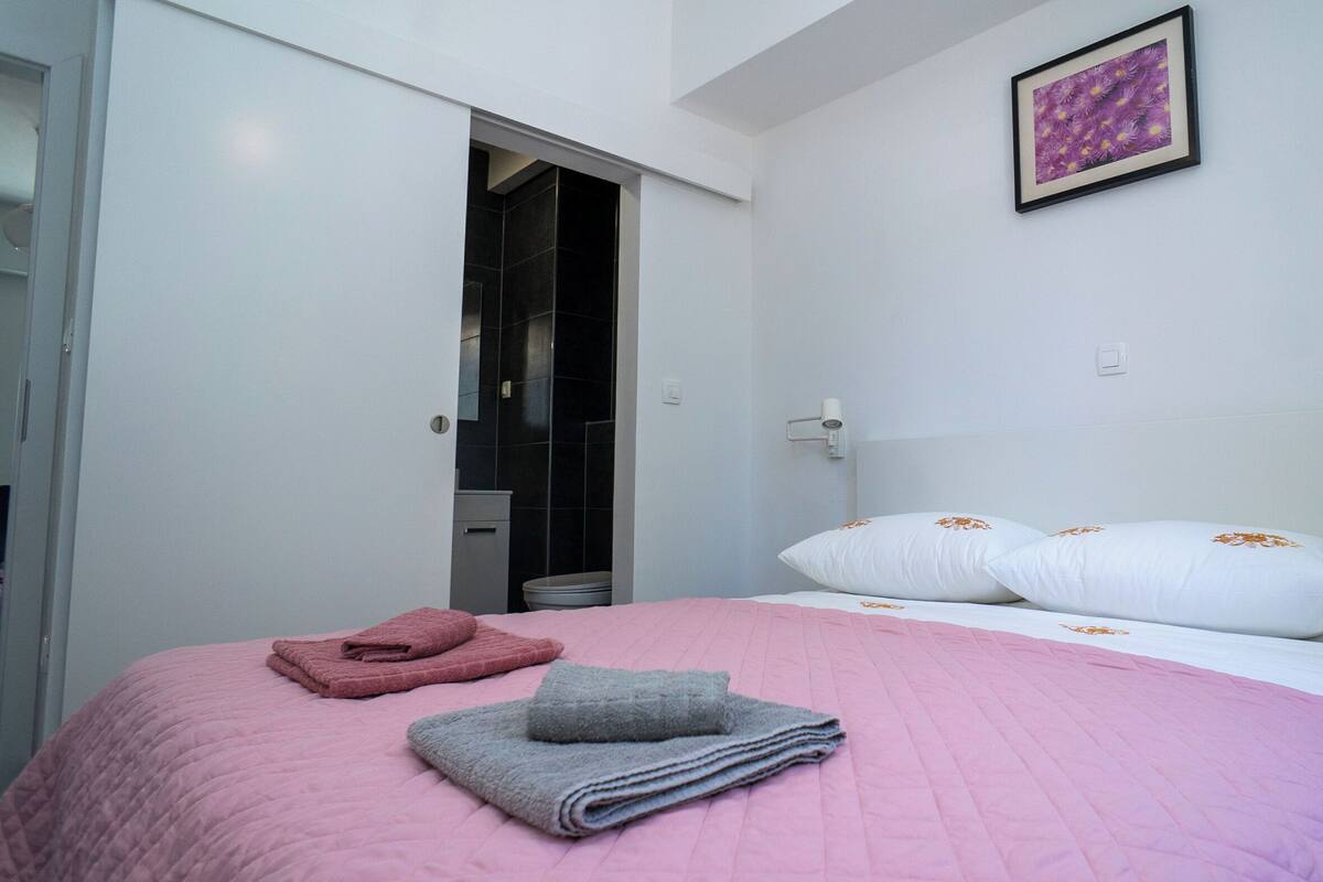 A bedroom with a bed, pillows, a framed picture, and a bathroom door.