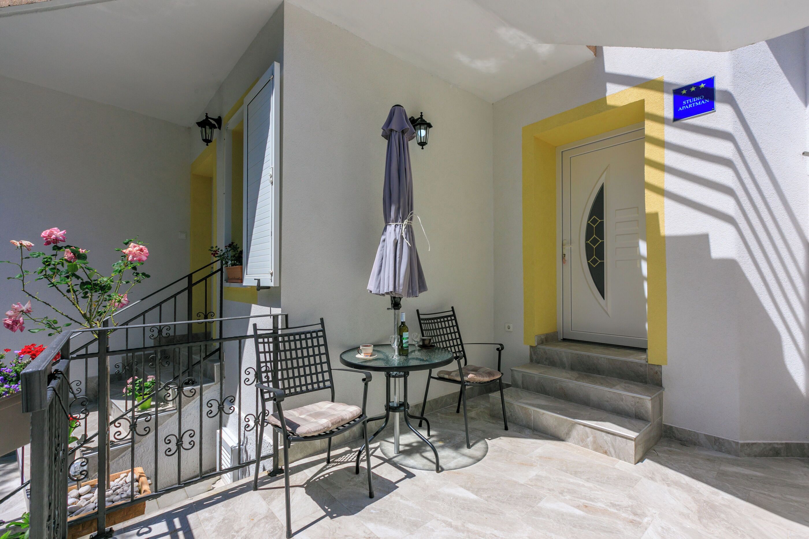 A balcony with a table, chairs, and a potted plant.