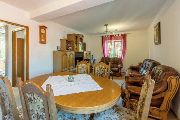 A dining area with a round wooden table, floral chairs, a brown leather sofa, a wooden cabinet, and a red curtain. - Apartments Tatjana (Novi Vinodolski)