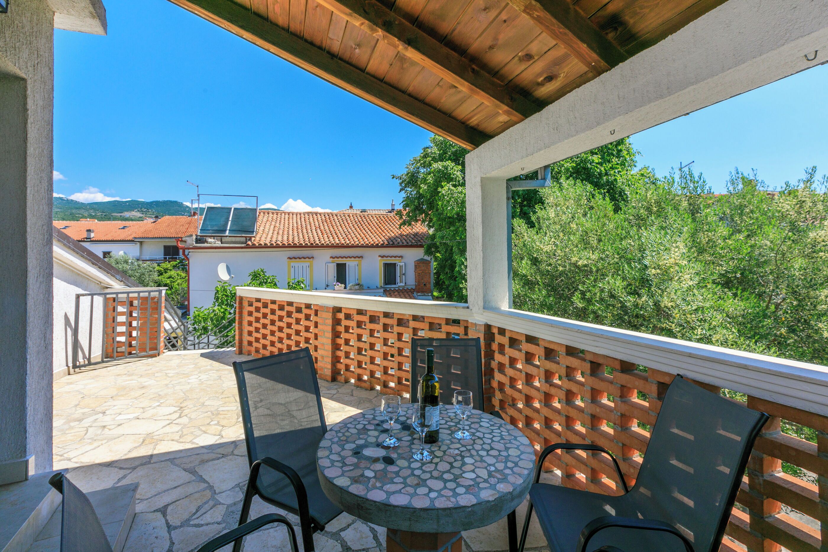 A covered outdoor patio with a round table, chairs, and a bottle of wine.