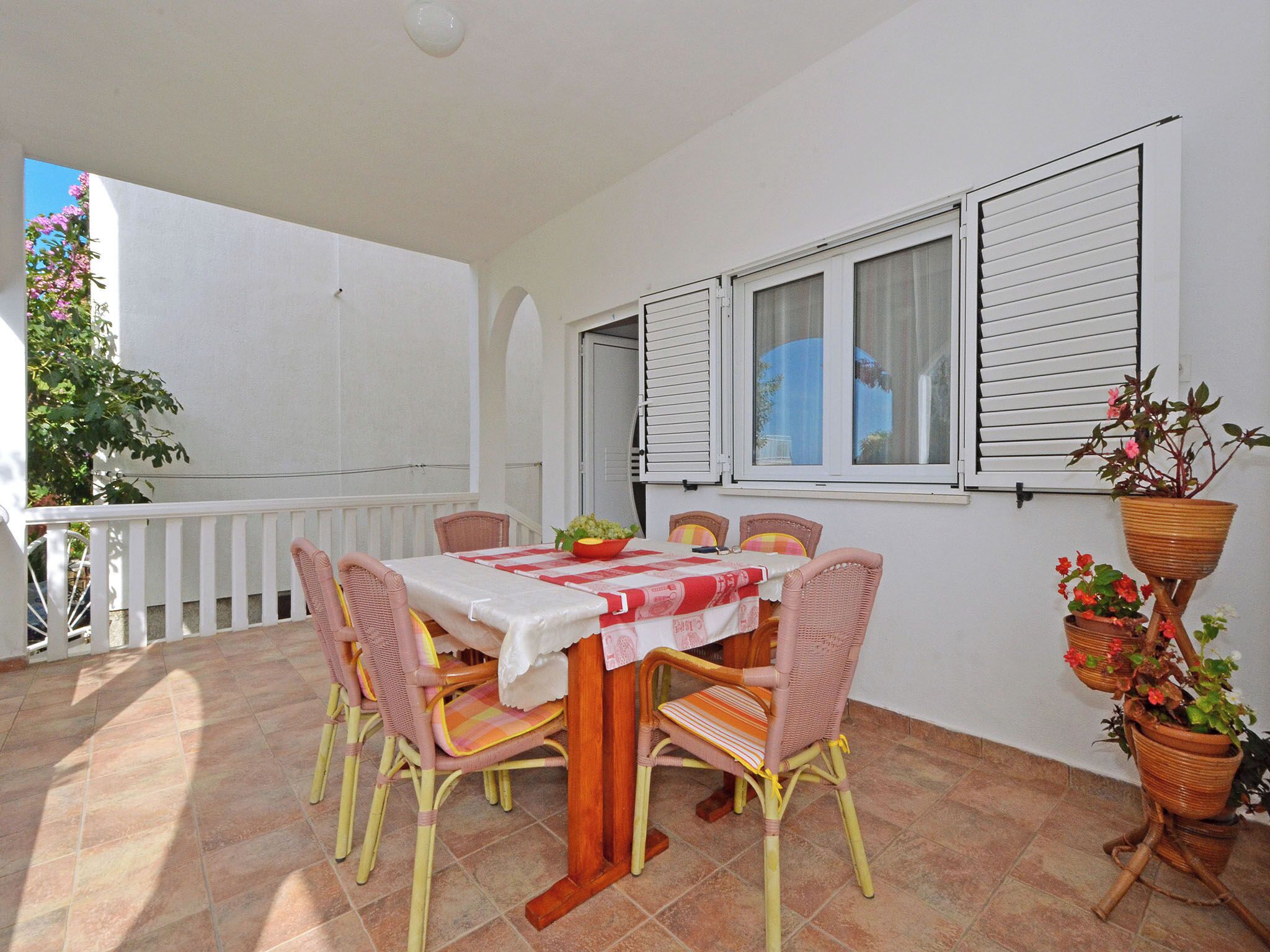 A covered outdoor dining area with a table set for four, surrounded by wicker chairs.