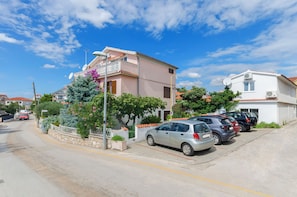 Una calle residencial con coches aparcados, una casa rosa con balcón y una casa blanca con tejado de baldosas.