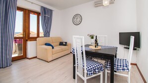 A furnished room with a sofa, dining table, chairs, a clock, and a TV. - Apartments Happy Place (Vodice)
