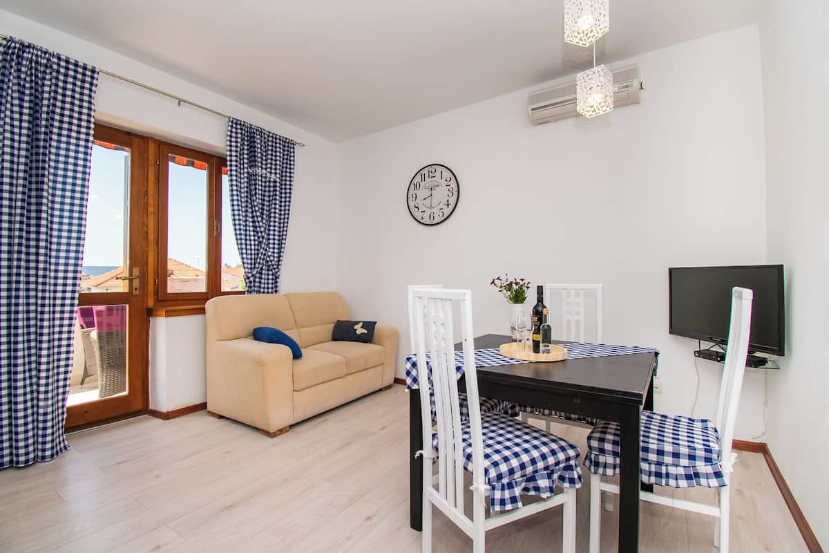 A furnished room with a sofa, dining table, chairs, a clock, and a TV.
