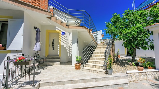 A residential building with a staircase leading to a second floor, outdoor seating area with a table and chairs, and potted plants. - Apartment Danijel (Novi Vinodolski)