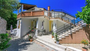 A two-story building with a staircase leading to a balcony. There are outdoor seating areas with tables and chairs. - Apartment Danijel (Novi Vinodolski)