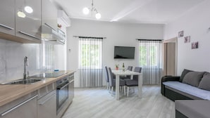 A modern kitchen with stainless steel appliances, a dining area with a table and chairs, and a living area with a sofa. - Apartment Danijel (Novi Vinodolski)