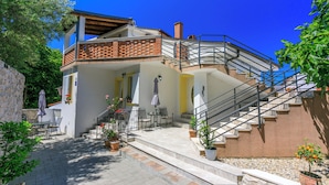 A two-story building with a staircase leading to a balcony. There are outdoor seating areas with tables and chairs. - Apartment Studio (Novi Vinodolski)