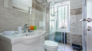 A modern bathroom with a white sink, toilet, and glass shower enclosure. - Apartment Studio (Novi Vinodolski)