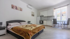 A modern bedroom with a large bed, a desk, a chair, and a kitchenette. - Apartment Studio (Novi Vinodolski)