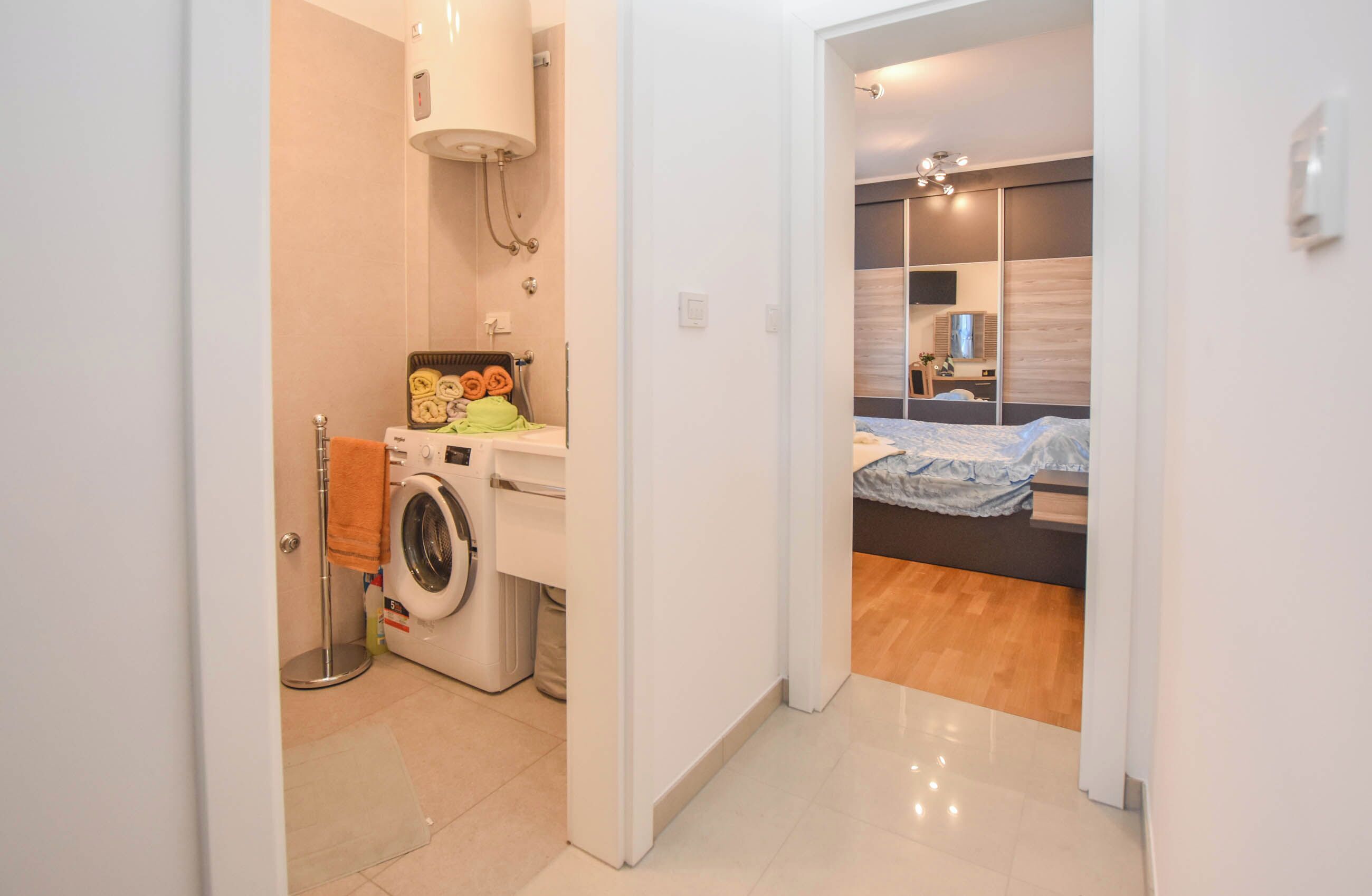 Una camera d'albergo moderna con lavatrice, un letto con copriletto blu e pavimento in legno.