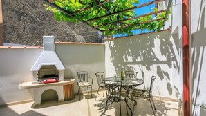 Een terras buiten met een pizzaoven, een ronde tafel en stoelen.