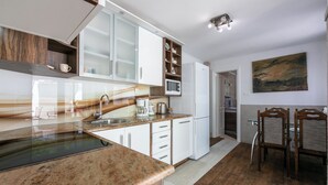 Een moderne keuken met witte kasten, een granieten aanrecht en een ingebouwde magnetron. Er is een eethoek met twee houten stoelen en een glazen tafel.