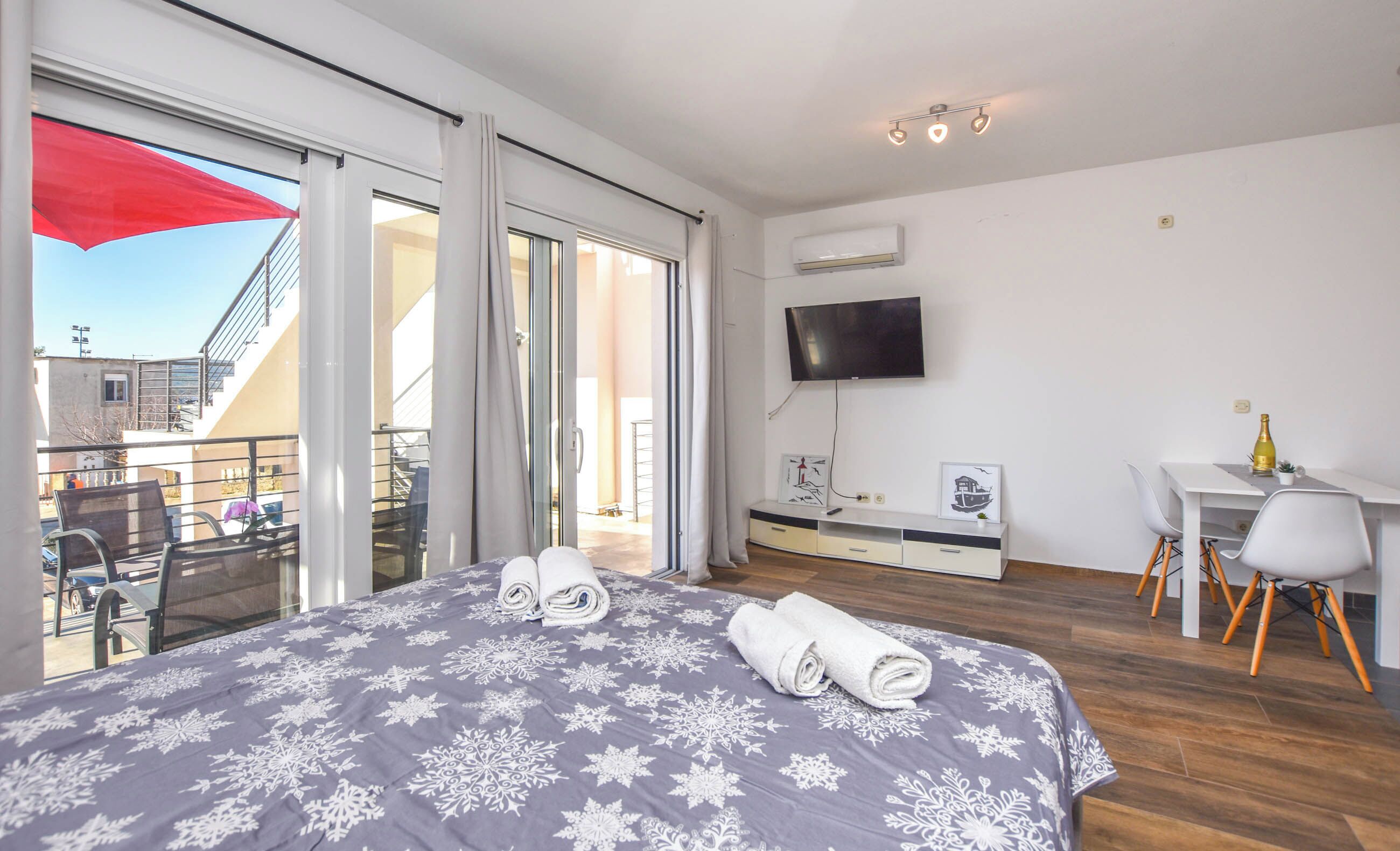 Habitación de hotel con cama, escritorio, televisor y balcón con sombrilla roja.