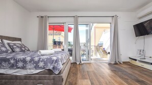 Una camera da letto con un letto, una televisione e un balcone con un ombrellone rosso.