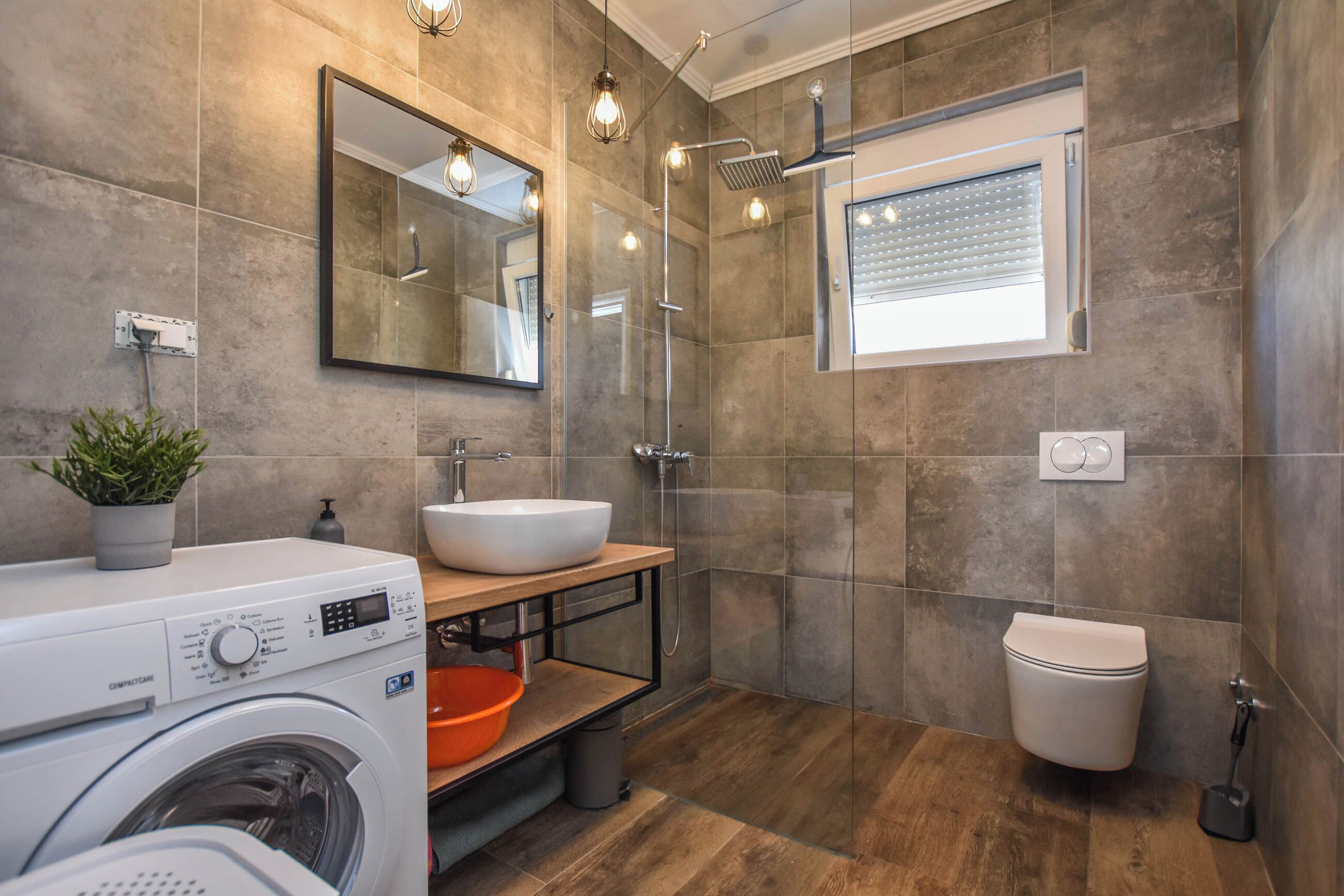 Een moderne badkamer met een wasmachine, een wastafel, een douche en een toilet.