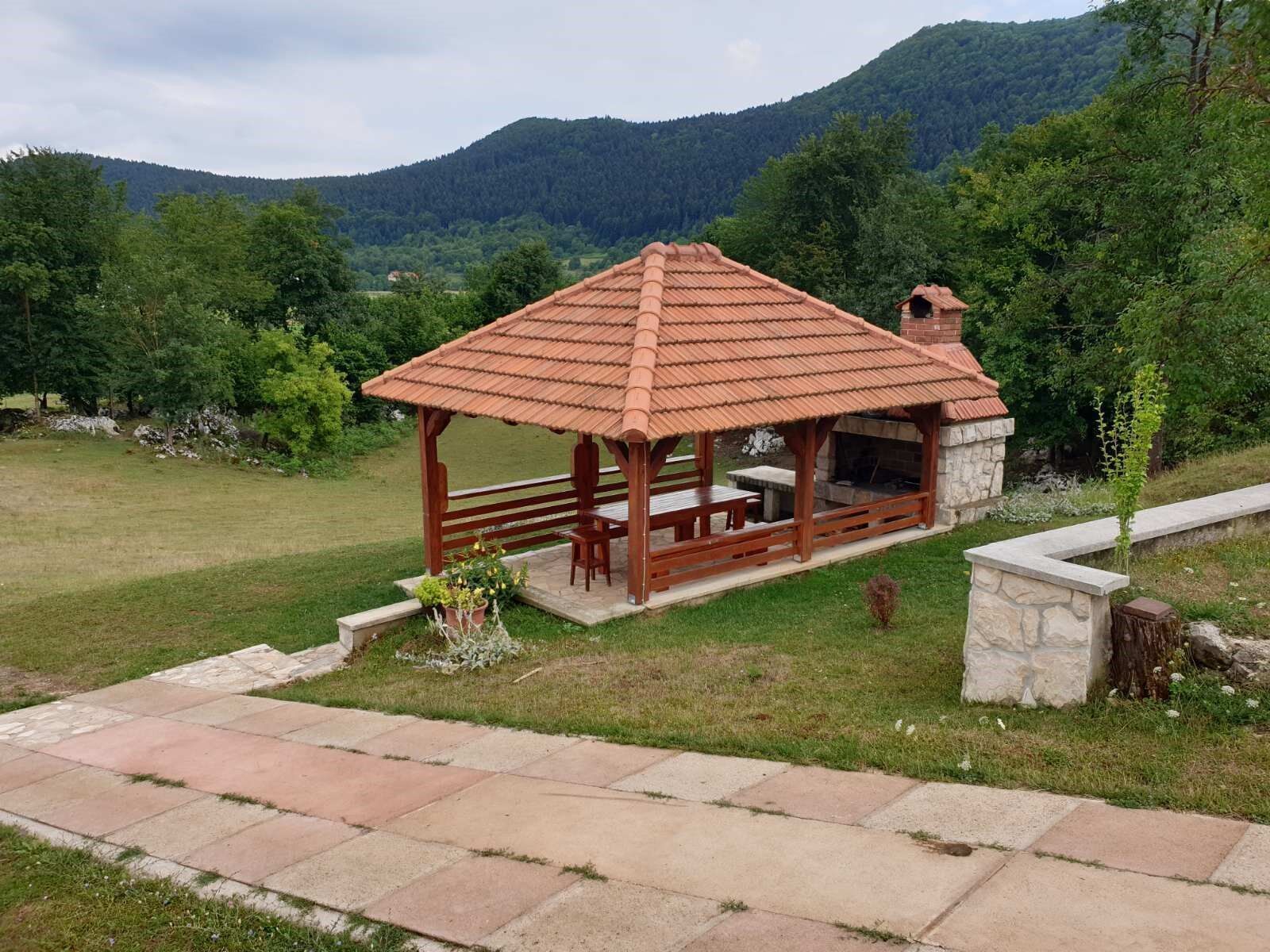 A wooden gazebo with a tiled roof, stone walls, and a stone fireplace.