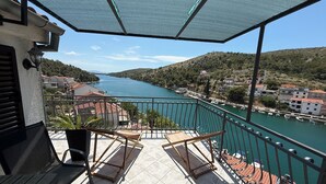 A balcony with a view of a river, a chair, and a potted plant. - Apartments Adriatico (Sibenik)