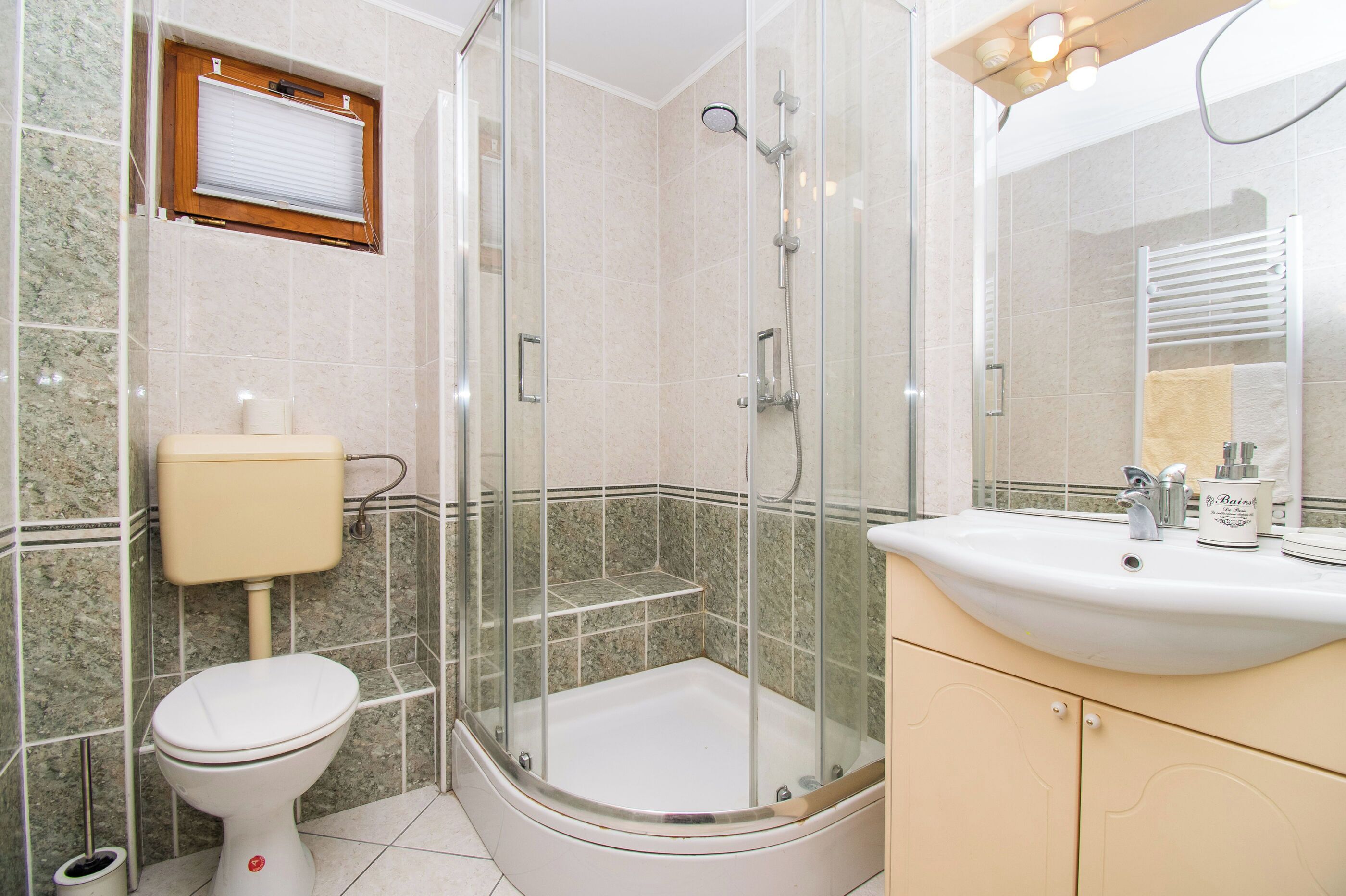 A bathroom with a glass-enclosed shower, a toilet, and a sink with a mirror.