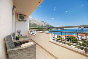 Ein Balkon mit Korbmöbeln, einem kleinen Tisch mit einer Pflanze und Blick auf Meer und Berge.